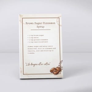Peut inclure: Un panneau rectangulaire &agrave; fond blanc avec une bordure marron portant le texte Brown Sugar Cinnamon Syrup, une liste de recettes avec des mesures en tasses et cuill&egrave;res &agrave; caf&eacute;, des instructions, la phrase Life begins after coffee et des grains de caf&eacute;.