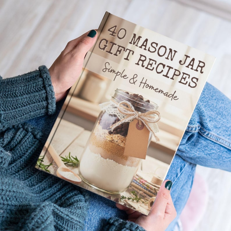 May include: A softcover book titled 40 Mason Jar Gift Recipes Simple & Homemade. The cover features a photograph of a glass jar filled with layered dry ingredients, adorned with a lace ribbon and a blank brown paper tag, resting on a wooden surface.