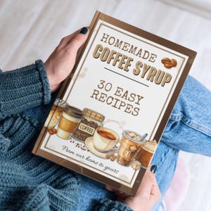 Peut inclure: Un livre reli&eacute; intitul&eacute; HOMEMADE COFFEE SYRUP 30 EASY RECIPES From our home to yours. La couverture pr&eacute;sente des illustrations de diverses boissons au caf&eacute;, un bocal de grains de caf&eacute; et une tasse sur une soucoupe sur fond blanc.