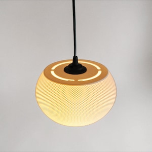 May include: A contemporary pendant light. The lampshade is spherical, textured, and off-white, with a dotted pattern. It hangs from a black cord and has a black base. The light emits a warm glow.