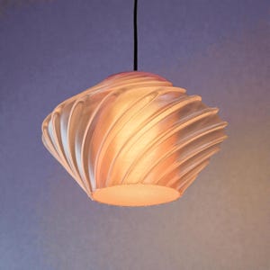 Könnte beinhalten: Eine Hängeleuchte mit einem einzigartigen, wirbelnden Design. Der cremefarbene, gerippte Schirm verjüngt sich nach unten. Die Leuchte hängt an einem schwarzen Kabel vor einem violett-gelben Farbverlauf. Die Leuchte ist ein dekoratives Element.