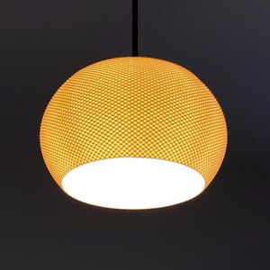 May include: A gold-colored pendant light with a round, textured shade. The shade is made of small, round holes that create a honeycomb pattern. The light is on and casting a warm glow.