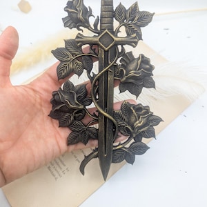 May include: A bronze decorative sword with a floral design. The sword has a detailed hilt and blade, intertwined with roses and leaves. The piece has an antique aesthetic.