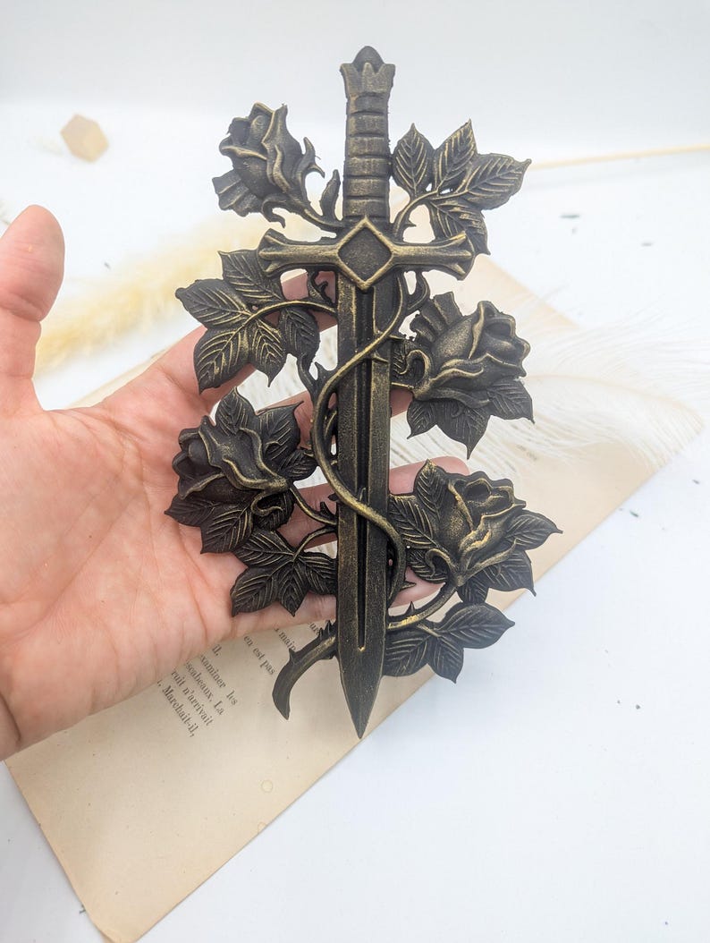 May include: A bronze decorative sword with a floral design. The sword has a detailed hilt and blade, intertwined with roses and leaves. The piece has an antique aesthetic.