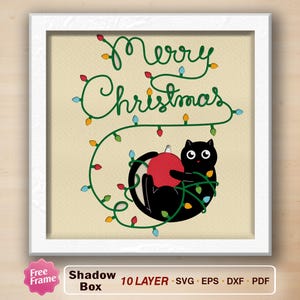 May include: A framed Christmas-themed shadow box design. The artwork features a black cat holding a red ornament, tangled in colorful Christmas lights. The words "Merry Christmas" are written in green script above.
