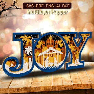 May include: A layered paper art piece spelling "JOY" in blue, white, and gold. The design features a nativity scene with palm trees, angels, and a star. The text "SVG PDF PNG AI DXF" and "Multilayer Papper" are at the top.