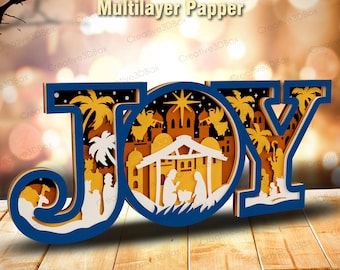 May include: A layered paper art piece spelling "JOY" in blue, white, and gold. The design features a nativity scene with palm trees, angels, and a star. The text "SVG PDF PNG AI DXF" and "Multilayer Papper" are at the top.