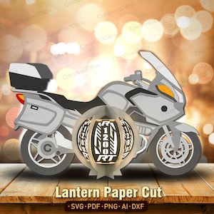 Könnte beinhalten: Ein Papierschnitt-Design eines Motorrads mit einer Laterne in der Mitte. Das Motorrad ist grau und weiß, mit einem schwarzen Staufach. Die Laterne trägt den Text "R 1200 RT". Der Text "Lantern Paper Cut" steht unten.