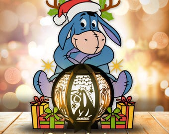 May include: A blue cartoon donkey wearing a red Santa hat and antlers sits on a black lantern with a Christmas scene. The lantern is surrounded by red and green gift boxes.