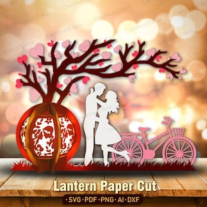 May include: A paper cut design featuring a red lantern, a tree with pink heart-shaped leaves, and a couple embracing. A pink bicycle is also included. The words "Lantern Paper Cut" are at the bottom.