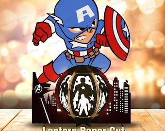 May include: A multi-layered paper cut lantern design featuring a cartoon Captain America with a shield above a city skyline silhouette. The central circular panel displays a cutout of a hero figure with a star, and the text Lantern Paper Cut.