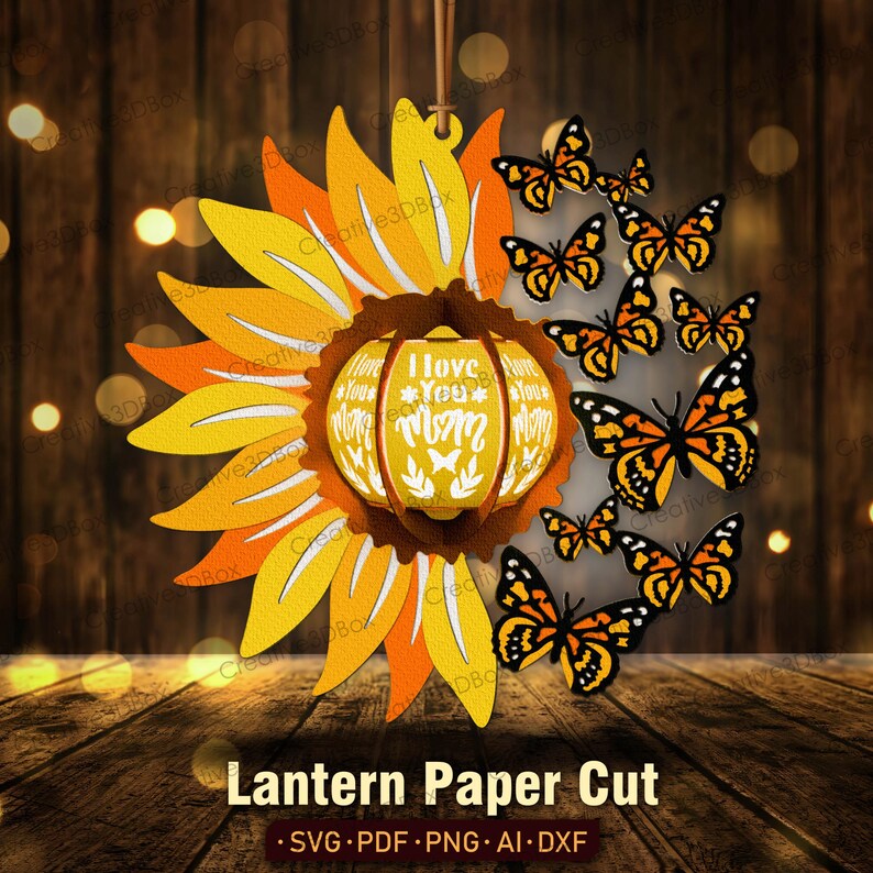 May include: A paper cut lantern design featuring a sunflower with a pumpkin-shaped center that reads "I Love You Mom". The lantern is surrounded by a ring of butterflies.