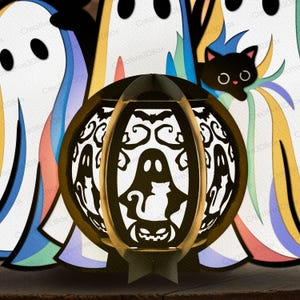 以下が含まれることがあります： ハロウィーンをテーマにした紙製のランタン。幽霊、猫、カボチャの切り抜きデザインが施されています。ランタンは茶色で中に光があり、幽霊と黒猫の切り絵に囲まれています。