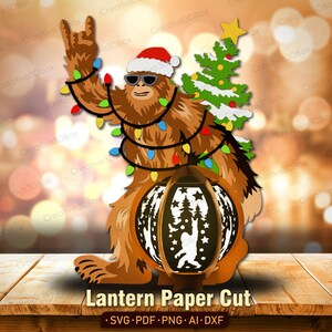 May include: A brown paper cut-out of a Bigfoot character wearing a Santa hat and sunglasses, holding a Christmas tree and a lantern. The lantern has a Bigfoot silhouette and forest scene. The text "Lantern Paper Cut" is at the bottom.
