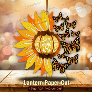 May include: A paper cut lantern design featuring a sunflower with a yellow and orange center and a pumpkin-shaped lantern with the text "I love you Mom" in the center. The lantern is surrounded by butterflies in shades of orange and brown.