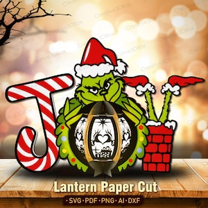 May include: A layered paper cut design featuring the Grinch character, a candy cane-striped letter "J", and a lantern. The Grinch wears a Santa hat and holds the lantern. The text "Lantern Paper Cut" is at the bottom.