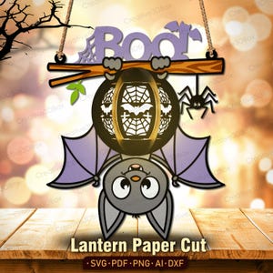 May include: A Halloween-themed paper cut design featuring a bat hanging upside down, holding a lantern with a bat and spider web design. The word "BOO" is above the bat. The design is suspended by a wooden beam and rope. The text "Lantern Paper Cut" is at the bottom.