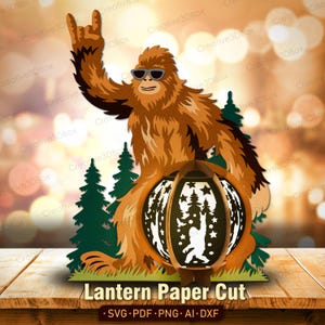 May include: A brown paper cut-out of a Bigfoot figure wearing sunglasses and giving a rock-on hand gesture. The figure is holding a lantern with a forest scene cut into it. The words "Lantern Paper Cut" are at the bottom.