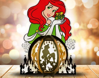 May include: A red-haired cartoon character holding a green gift box, standing above a wooden lantern with a silhouette of a cartoon character inside. The lantern is decorated with stars and snowflakes. The text "Cartoon Lantern" is below the lantern, with the text "SVG. PDF. PNG. AI. DXF" below that.