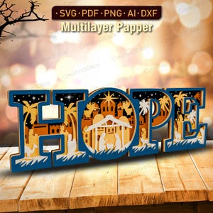 May include: A layered wooden art piece spelling "HOPE" in blue, with a nativity scene and palm trees inside the letters. The artwork is on a wooden surface and includes the text "SVG PDF PNG AI DXF" and "Multilayer Papper".