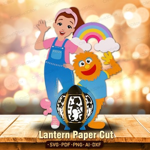 May include: A vibrant paper cut design showing a girl, an orange monster, and a rainbow. It includes a black lantern with cut-out figures and the text "Lantern Paper Cut". The figures are on a wooden surface.
