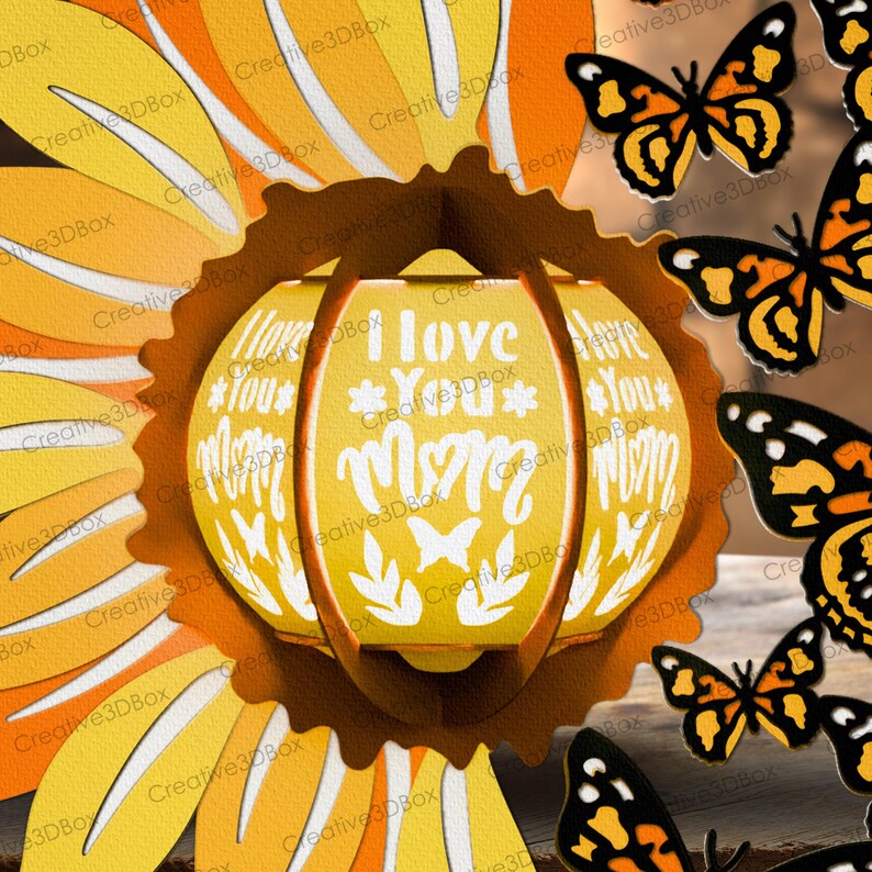 May include: A yellow and orange paper craft sunflower with a 3D paper lantern in the center. The lantern is white with the words "I love you Mom" written on it. There are butterflies around the sunflower.