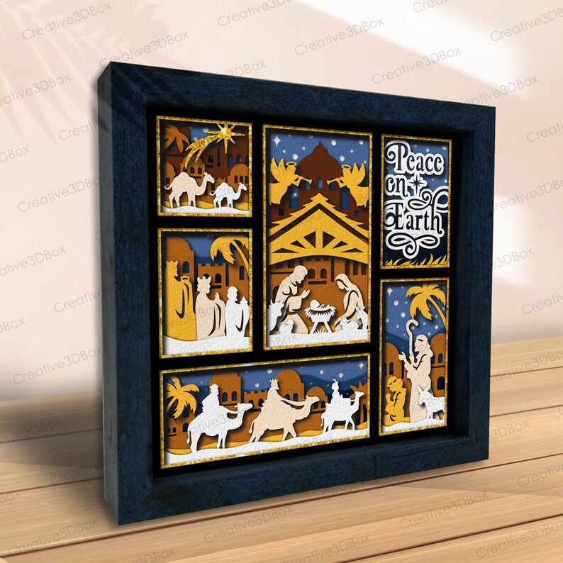 May include: A framed, multi-layered paper art piece depicting scenes from the Nativity. The artwork features camels, the three wise men, angels, and the text "Peace on Earth." The frame is dark blue, and the artwork has a warm color palette.