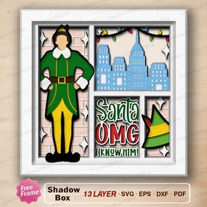 May include: A layered shadow box featuring a green and yellow elf character, a cityscape, and the text "Santa OMG I KNOW HIM!". The artwork includes a green elf hat and string lights, all within a white frame.