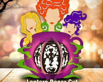 May include: A paper cut design featuring three stylized witch figures with orange, yellow, and purple hair, above a purple cauldron-shaped lantern. The lantern has a cut-out design with silhouettes. The text "Lantern Paper Cut" is at the bottom.