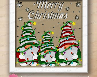May include: A framed Christmas shadow box featuring three gnomes with striped hats, wrapped in string lights. The words "Merry Christmas" are cut out at the top. The gnomes have white beards and are in front of a tan background.