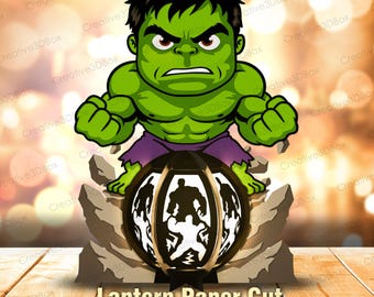 May include: A layered paper cut lantern design featuring a green muscular character with dark hair and purple shorts standing above a circular structure. The circular base displays a silhouette of the same character. Text reads Lantern Paper Cut.