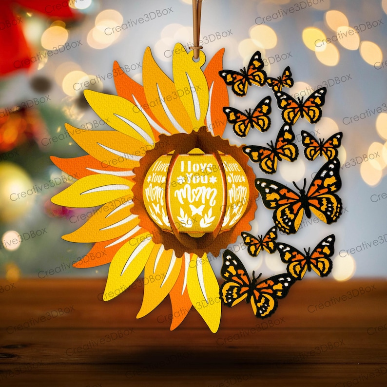 May include: A wooden ornament shaped like a sunflower with a yellow and orange color scheme. The center of the sunflower is a round, wooden lantern with the words "I Love You Mom" on it. The ornament is surrounded by butterflies with orange and black wings.
