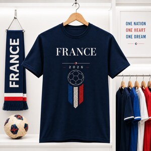 May include: Navy blue t-shirt with "FRANCE" printed in white, a soccer ball graphic, and the year "2026". A scarf with "FRANCE" in white and a soccer ball are also visible. The theme is soccer.