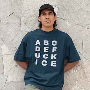 May include: A dark teal t-shirt with the word "ABC DEF UCK ICE" printed in white. The shirt is worn by a person wearing a black baseball cap. The person is leaning against a stone wall.