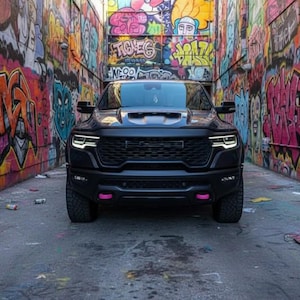 May include: A black pickup truck with pink accents is parked in an alley. The alley walls are covered in colorful graffiti art. The truck's headlights are illuminated, and the scene is lit with natural light.