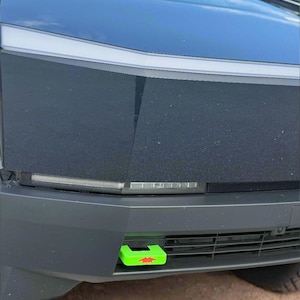 Puede incluir: Un gancho de remolque verde con un diseño de estrella roja está unido al parachoques delantero de un coche negro.