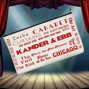Könnte beinhalten: Eine weiße Canvas-Reißverschlusstasche mit rotem Text, der Broadway-Musicals wie "Cabaret" und "Chicago" auflistet. Die Tasche wird vor einem Bühnenhintergrund mit roten Vorhängen präsentiert.
