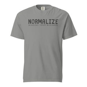 Puede incluir: Una camiseta gris con las palabras "NORMALIZE" sobre "MINDING YOUR BUSINESS" en letras negras. La camiseta es de cuello redondo y manga corta.