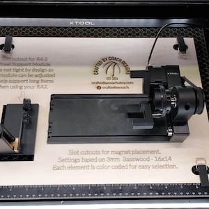 Puede incluir: Una base de madera cortada con láser con componentes negros, incluido un módulo de soporte de rueda y otras piezas. El texto en la base describe los componentes y su función. La base está diseñada para el módulo de soporte de rueda RA2.