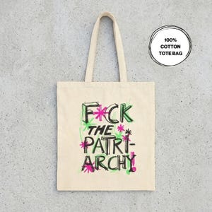 以下が含まれることがあります： 「F*CK THE PATRIARCHY」と書かれた黒、緑、ピンクのテキストが入ったクリーム色のトートバッグ。バッグは長方形の形とハンドルが付いたシンプルなデザインです。テキストは手書き風です。「100% COTTON TOTE BAG」と書かれた円形のグラフィック。