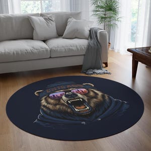 May include: Round navy blue rug featuring a detailed illustration of a bear wearing sunglasses and a Chicago beanie. The bear has an open mouth, showing its teeth. The rug is placed on a hardwood floor in a living room setting.