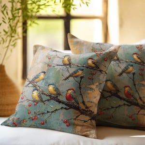 May include: Two square throw pillows featuring a printed illustration of multiple small birds perched on dark, leafless branches with red berries against a textured, muted blue and beige background. The fabric displays a painterly art style.