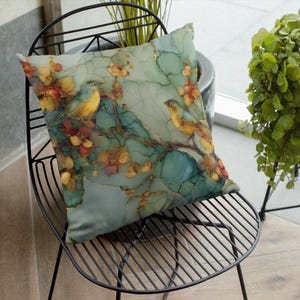 May include: Square decorative pillow featuring a watercolor design of two birds perched on a flowering branch. The pillow has a teal background with gold accents and colorful flowers in shades of red, orange, and yellow.