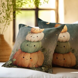 May include: Two square throw pillows featuring a stacked illustration of four smiling pumpkins in orange, green, white, and light orange colors. The background depicts a dark teal night sky with small yellow stars and green foliage at the base.