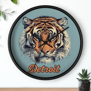 May include: A black framed clock with a blue background featuring a tiger face illustration and the word "Detroit" in orange text.