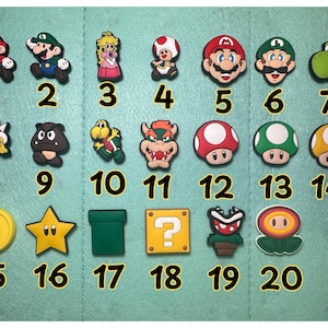 Può includere: Una collezione di 20 ciondoli colorati in stile cartone animato con personaggi e icone della serie di videogiochi Super Mario. Include Mario, Luigi, la Principessa Peach, Toad, Yoshi e altri elementi riconoscibili.