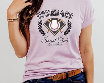 May include: A pink t-shirt with a baseball-themed graphic that says "Homebase Social Club Loud and Proud".