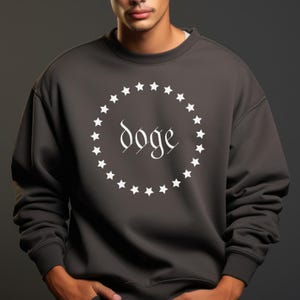 May include: Dark gray sweatshirt with a white circular design of stars around the word "Doge" in a stylized font. The sweatshirt is a solid color and has a crew neck.