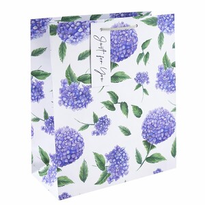 May include: A white gift bag patterned with purple hydrangea flowers and green leaves. The bag has a tag with the words "Just for You" in black script and a silver cord handle.