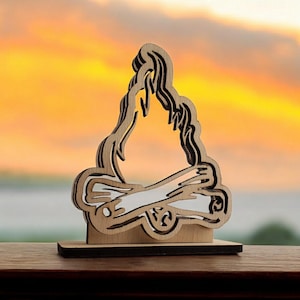 May include: Wooden cutout of a campfire with a flame and logs. The cutout is on a wooden base with a black edge.